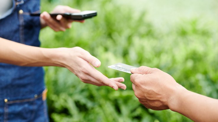 One person hands over his credit card to another, in the background is a green meadow