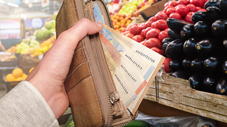 Aus einer Geldbörse schauen Geldscheine heraus vor dem Hintergrund einer Gemüseabteilung