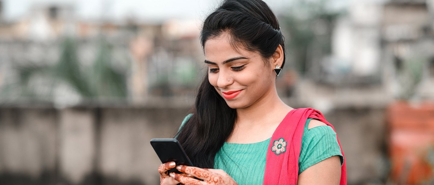 A Bangladeshi woman smiling at her smartphone