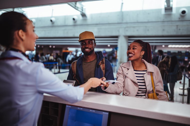 A smiling man and woman check in for their flight while an airport attendant passes the woman her passport and boarding pass.