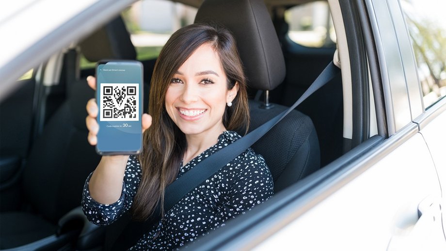 Woman in a car holding a smart phone displaying a QR code