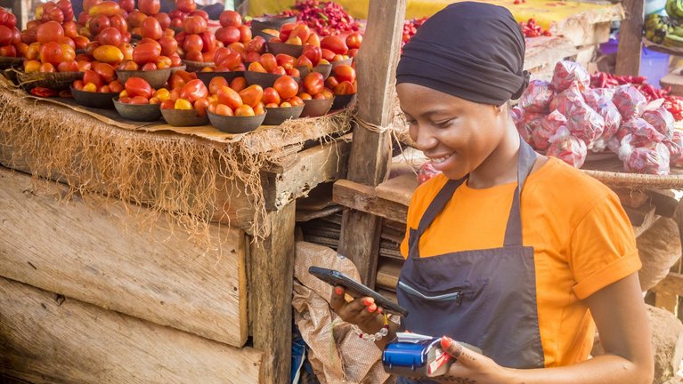A woman in a headscarf and apron operates a smartphone and a credit card payment device