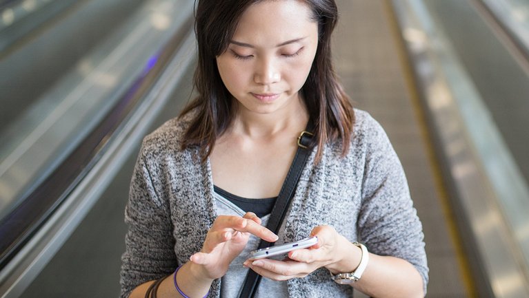 A woman rides an escalator and uses her smartphone