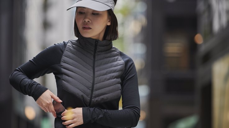 Frau in Sportkleidung steckt Kreditkarte aus Metall in ihre Jackentasche