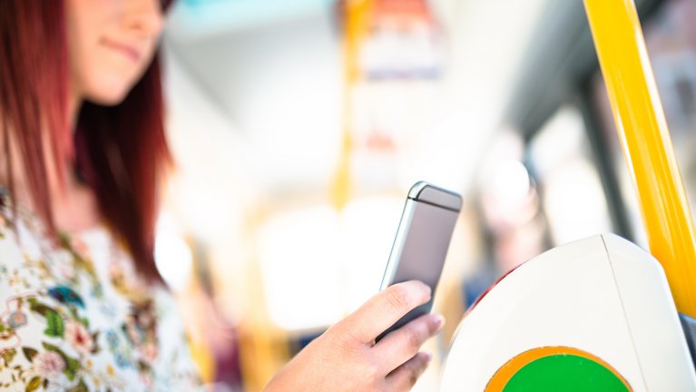 Eine Frau bezahlt in einem öffentlichen Verkehrsmittel ihr Ticket kontaktlos mit dem Smartphone