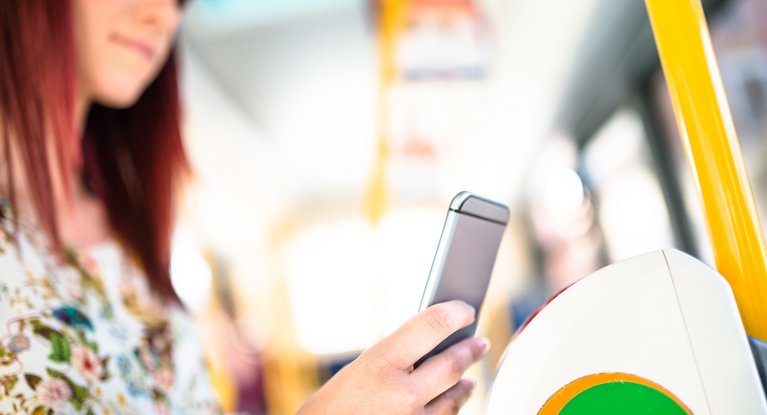 Eine Frau bezahlt in einem öffentlichen Verkehrsmittel ihr Ticket kontaktlos mit dem Smartphone