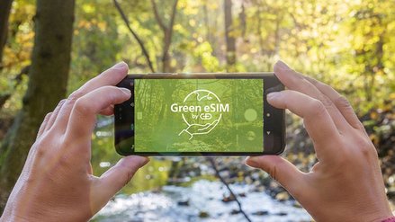 Smartphone mit dem G+D Green eSIM Logo vor bewaldeten Hintergrund