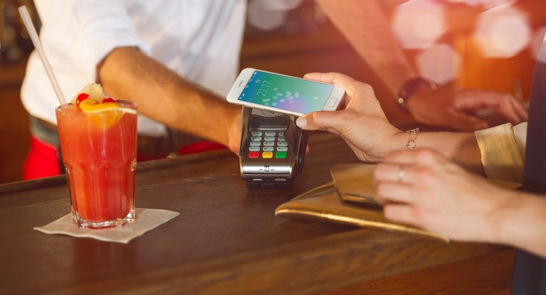 A woman pays contactless for her cocktail at a bar with her smartphone