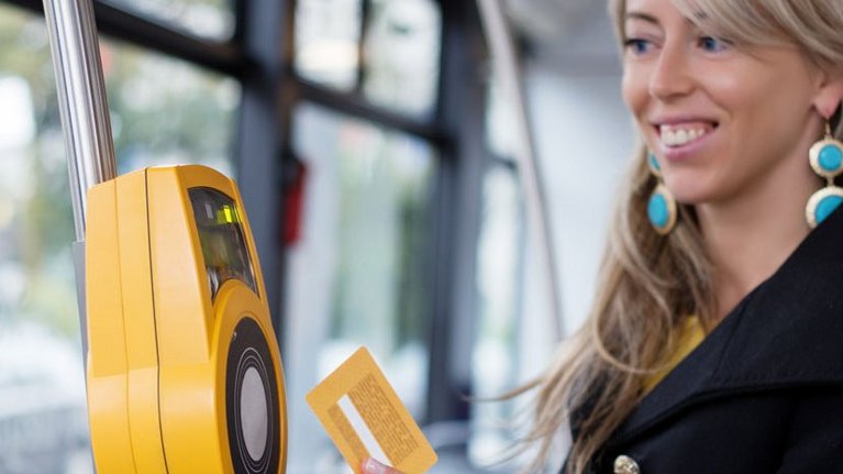 Eine Frau bezahlt mit einer Karte kontaktlos in einem öffentlichen Verkehrsmittel