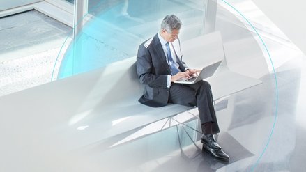 man in suit sits on a bank and types into his laptop