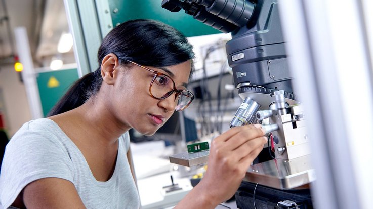 A young woman operates a microscope