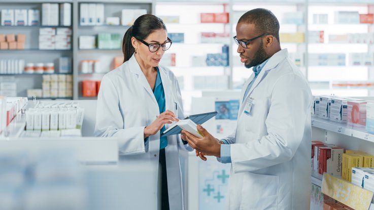 Two pharmacists talk to each other and operate a tablet
