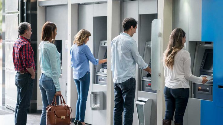Einige Personen stehen nebeneinander an Geldautomaten