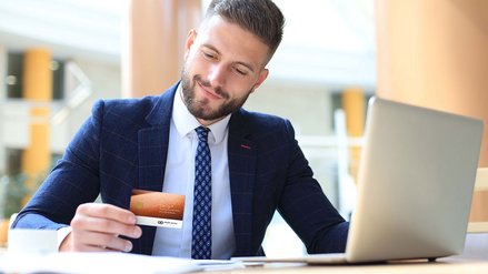 Ein lächelnder Geschäftsmann sitzt vor seinem Laptop und hält eine Kreditkarte in der Hand