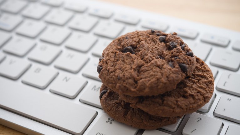 Two chocolate chip cookies lying on a computer keyboard