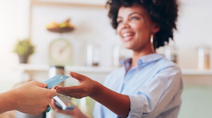 Eine lachende Frau mit einem Kartenlesegerät nimmt eine Kreditkarte entgegen 
