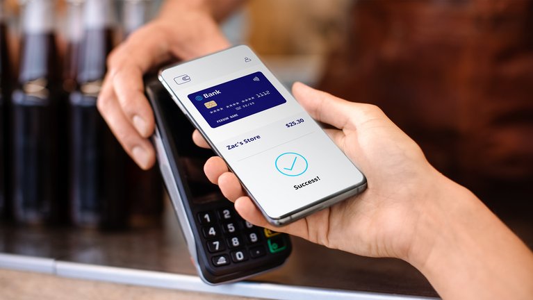 Nahaufnahme der Hand einer Person, die ein Smartphone mit einem Bildschirm mit erfolgreicher Zahlungsbestätigung über einem Zahlungsterminal hält.