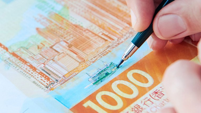 Eine Person zeichnet mit einem Stift auf einer Banknote mit asiatischen Schriftzeichen 