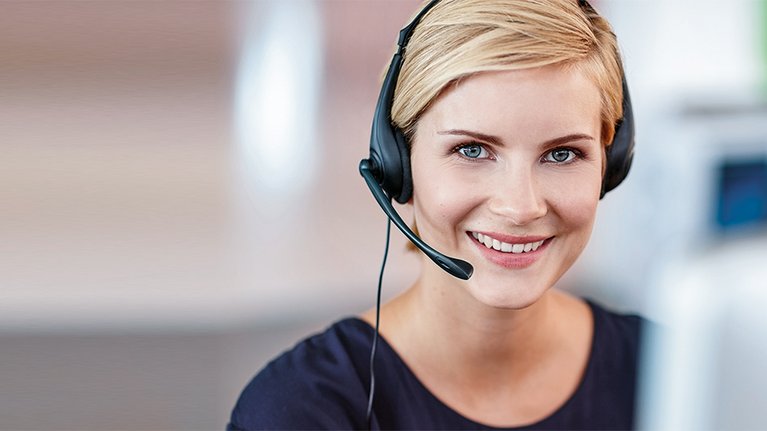 Smiling woman with a headset sits in front of a computer