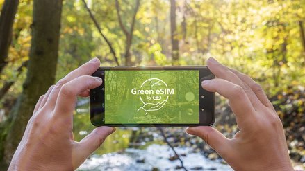 Smartphone mit dem G+D Green eSIM Logo vor bewaldeten Hintergrund 