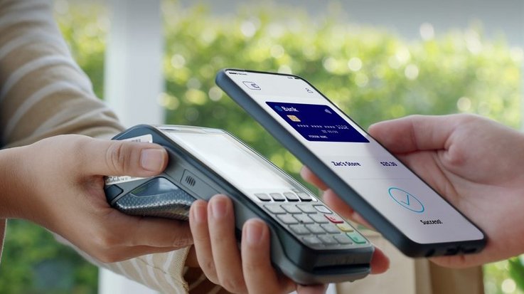 Eine Person bezahlt kontaktlos mit ihrem Smartphone, auf dem Screen erscheint die Abbildung einer Kreditkarte 
