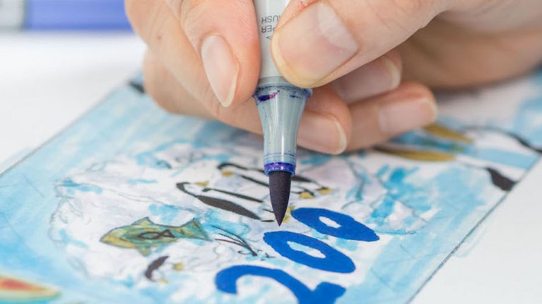 Jemand zeichnet mit blauem Filzstift eine Banknote mit Pinguin-Motiv
