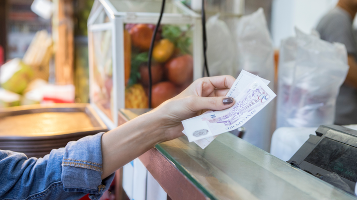 Eine Frau bezahlt mit Geldscheinen an einem Verkaufsstand