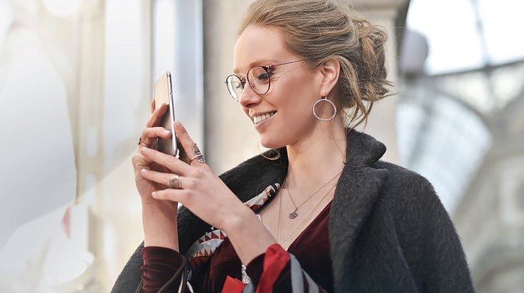 Smiling woman with a coat over her shoulders operates a smartphone