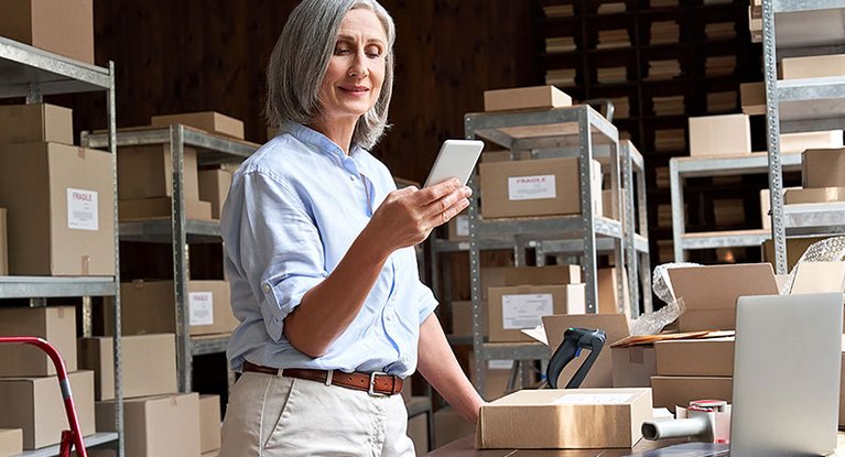 A woman stands in a storage room and uses her smartphone