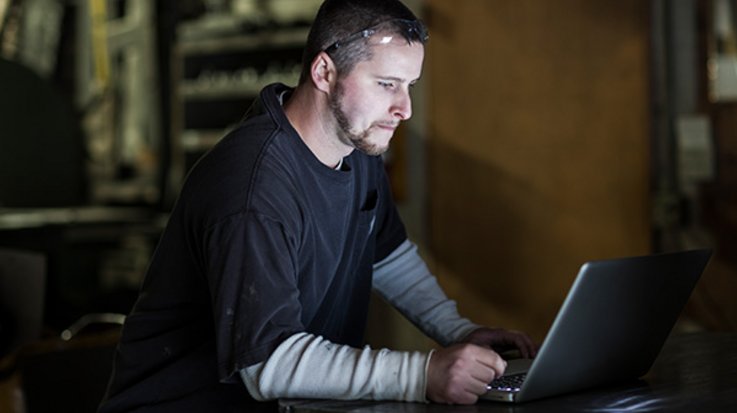 Ein Mann mit hochgeschobener Brille sitzt an einem Laptop und schaut auf das Display