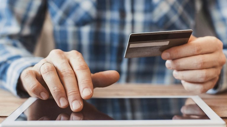 Ein Mann bedient ein Tablet und hält in der anderen Hand eine Kreditkarte