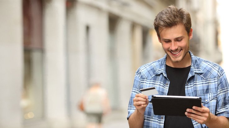 A young man holds a tablet and a credit card in his hands
