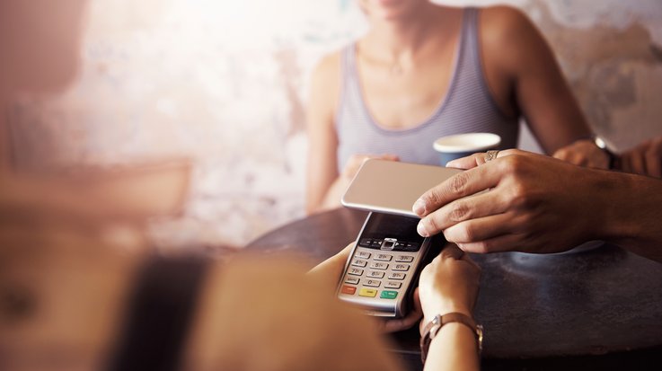 Eine Person bezahlt in einem Café kontaktlos mit dem Smartphone