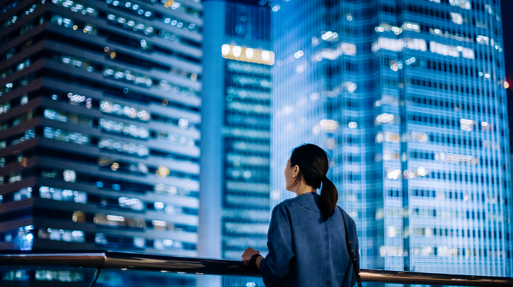 Image of woman from behind looking at illuminated skyscrapers