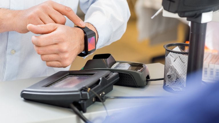 Ein Mann bezahlt kontaktlos mit seiner Smartwatch an einer Kasse