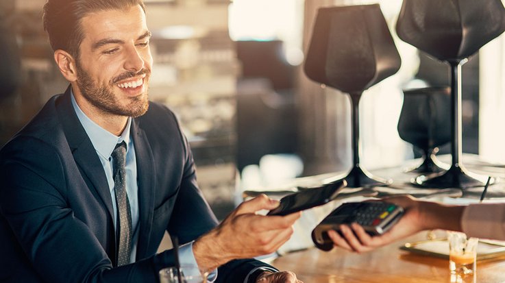 Ein lächelnder Geschäftsmann bezahlt in einem Restaurant kontaktlos mit seinem Smartphone