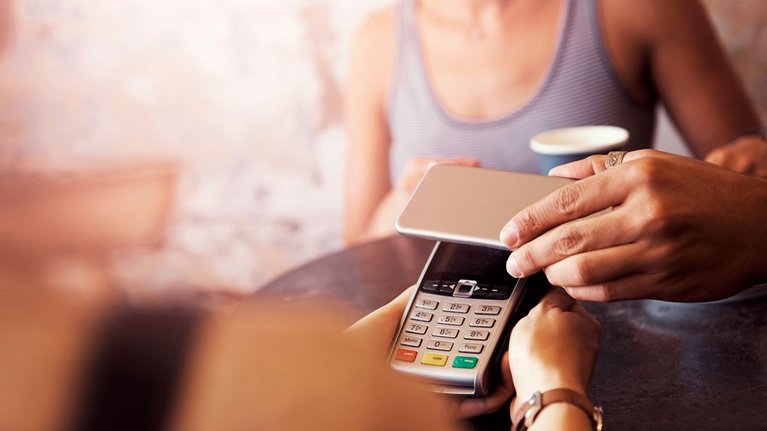 Eine Person bezahlt in einem Café kontaktlos mit dem Smartphone