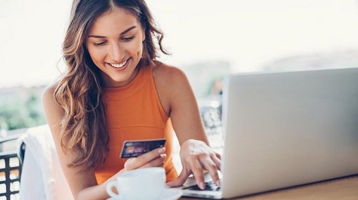 Lächelnde Frau bedient ihren Laptop und hält eine Kreditkarte in der anderen Hand