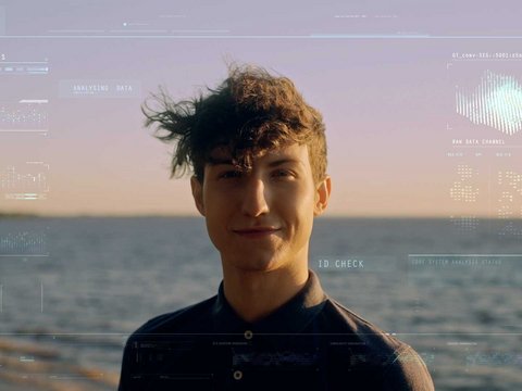 Ein Mann am sonnigen Strand blickt direkt in die Kamera, während biometrische Scandaten auf seinem Gesicht und im Hintergrund eingeblendet werden.