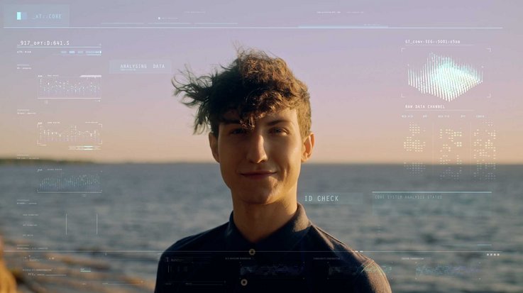 A man on a sunny beach looks into the camera with biometric scan data intricately displayed on his face and the backdrop.