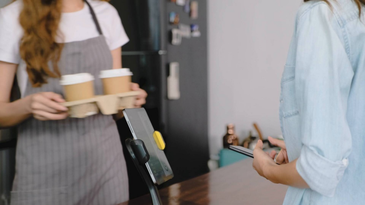 An einem Verkaufstresen wird mit dem Smartphone kontaktlos für zwei Kaffees bezahlt