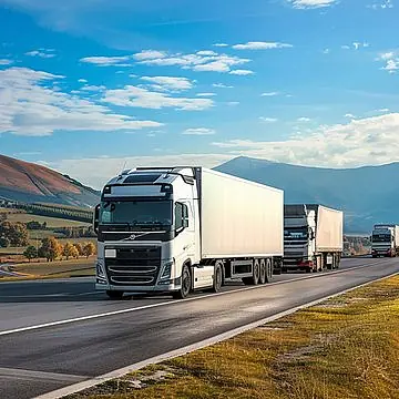 Convoy of white commercial trucks driving on an open highway.