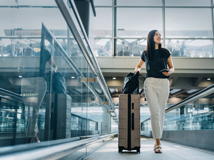 Junge asiatische Frau mit Reisepass und Koffer in der Flughafenhalle
