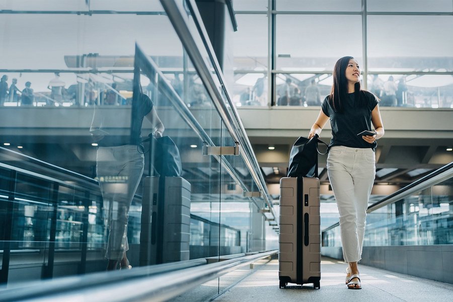 Junge asiatische Frau mit Reisepass und Koffer in der Flughafenhalle