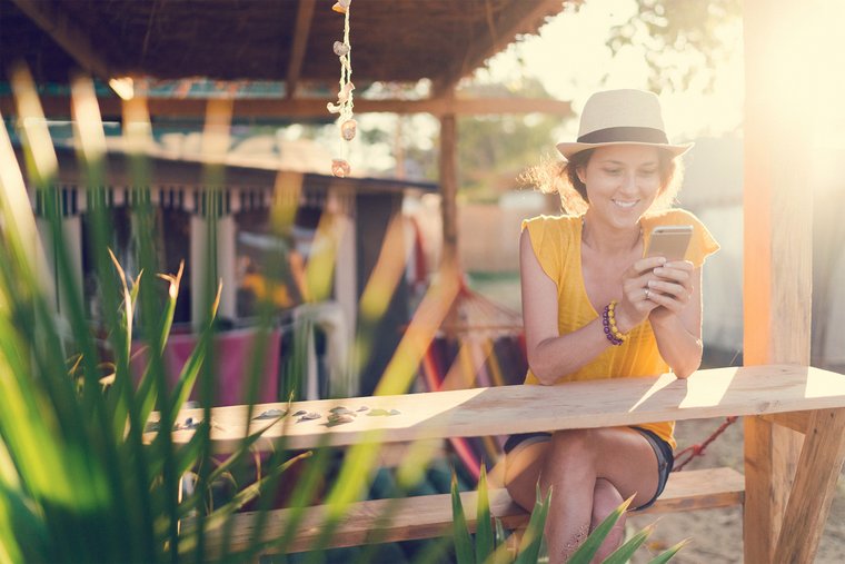 Junge Frau schaut auf ihr Handy auf einem Campingplatz, sommerliche Umgebung