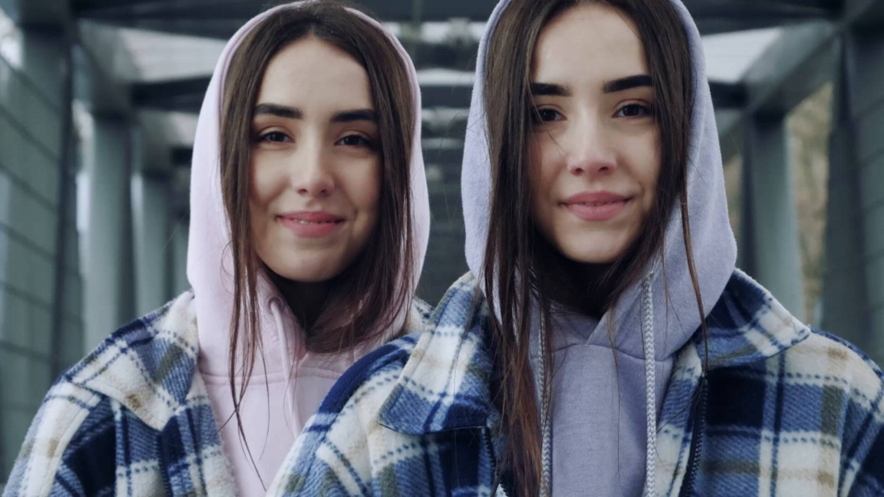 Ein junges weiblichen Zwillingspaar mit Hoodies lächelt geradeaus in die Kamera
