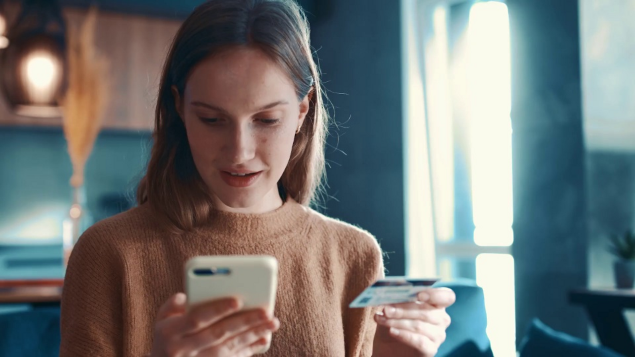 Eine junge Frau tippt die Daten ihrer Kreditkarte in ihr Smartphone ein