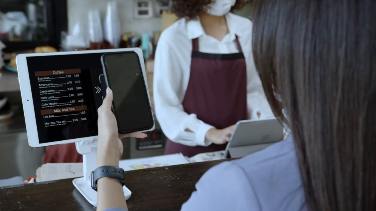 Eine Frau bezahlt kontaktlos mit ihrem Smartphone für zwei Kaffees an einem Tresen