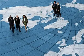 Business professionals walking across a large outdoor plaza with a world map.