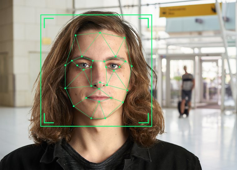 Grüne Gesichtserkennungsmarkierungen auf dem Gesicht eines langhaarigen jungen Mannes in einem Flughafengebäude